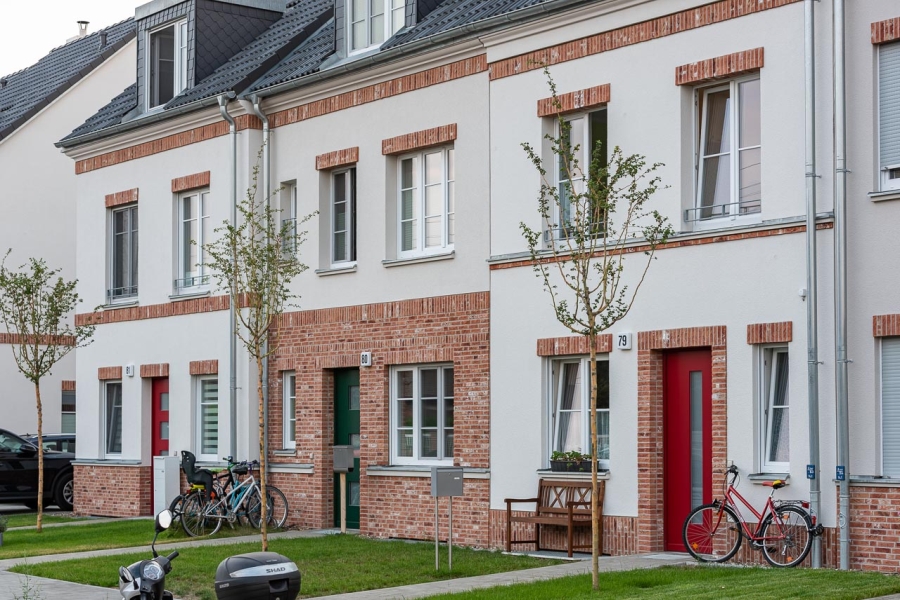 Grüne Aue Biesdorf Blick auf Fassaden dreier Reihenhäuser mit unterschiedlicher Fassadengestaltung. Außen rote Eingangtüren, in der Mitte eine grüne.
