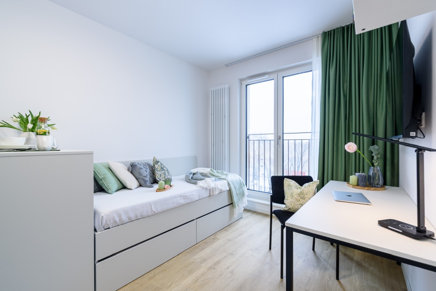Bett und Schreibtisch in möbliertem Zimmer mit großem Fenster